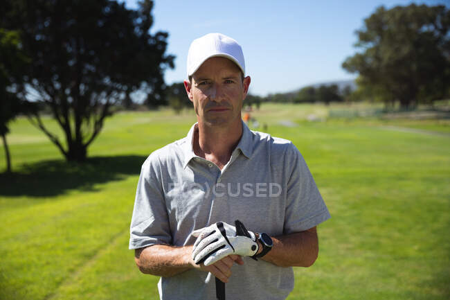 Портрет белого человека на поле для гольфа в солнечный день с голубым небом, держащего клюшку для гольфа, смотрящего в камеру — стоковое фото