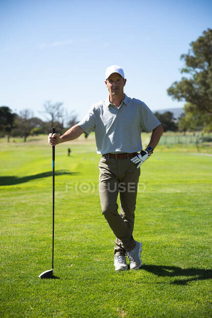 Портрет кавказького чоловіка на полі для гольфу в сонячний день з блакитним небом, тримаючи гольф клуб, дивлячись на камеру — стокове фото