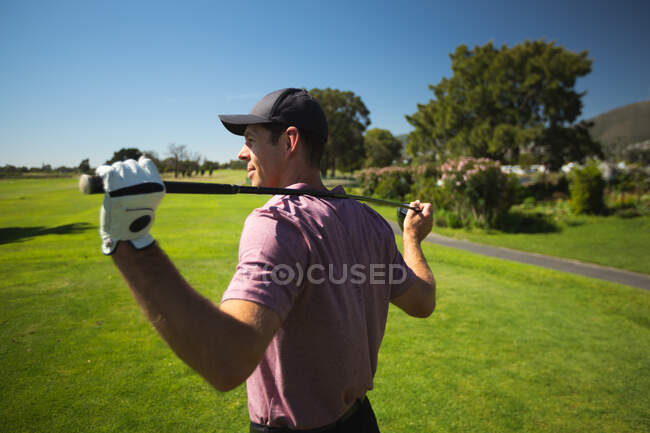 Вид сбоку на белого человека на поле для гольфа в солнечный день с голубым небом, держащего клюшку для гольфа через плечи — стоковое фото