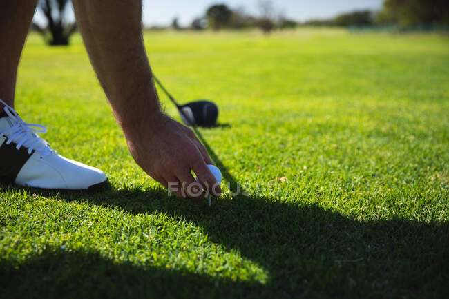 Низька частина людини на полі для гольфу в сонячний день, розміщуючи м'яч для гольфу на трійнику — стокове фото