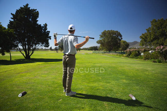Vue arrière d'un homme caucasien sur un terrain de golf par une journée ensoleillée avec un ciel bleu, tenant un club de golf sur ses épaules — Photo de stock