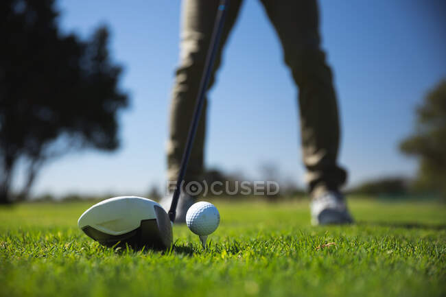 Низька частина людини на полі для гольфу в сонячний день з блакитним небом, готуючись вдарити м'яч для гольфу — стокове фото