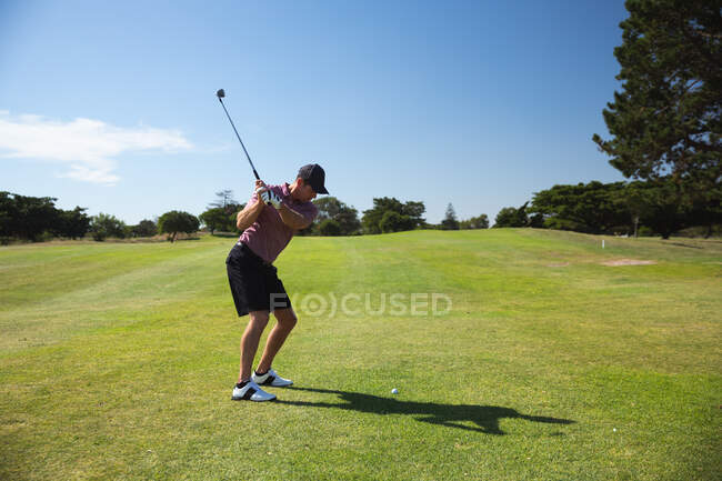 Вид спереди на кавказца на поле для гольфа в солнечный день с голубым небом, готовящегося ударить мячом для гольфа — стоковое фото