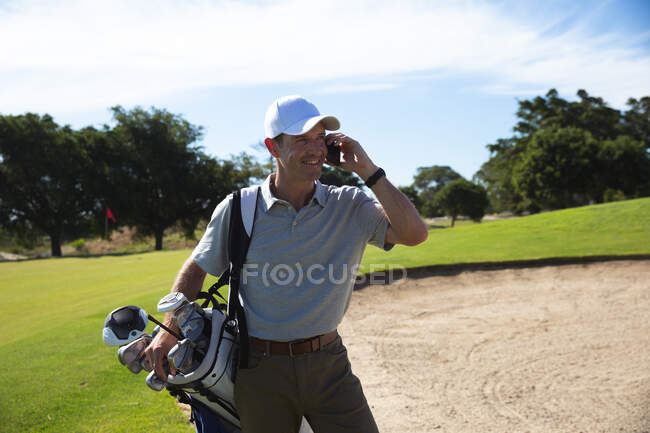 Вид спереди кавказца на поле для гольфа в солнечный день с голубым небом, разговаривающего по смартфону — стоковое фото
