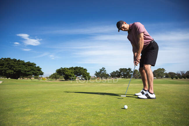 Vue latérale d'un homme caucasien sur un terrain de golf par une journée ensoleillée avec un ciel bleu, frapper une balle de golf — Photo de stock
