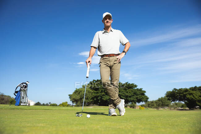 Портрет кавказького чоловіка на полі для гольфу в сонячний день з блакитним небом, спираючись на гольф клуб, дивлячись на камеру — стокове фото