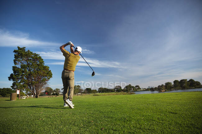 Vue arrière d'un homme caucasien sur un terrain de golf par une journée ensoleillée avec un ciel bleu, frapper une balle de golf — Photo de stock