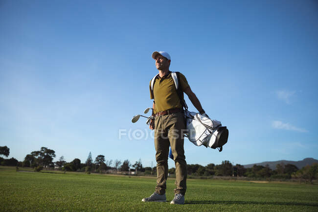 Вид спереди на белого человека на поле для гольфа в солнечный день с голубым небом, стоящего с сумкой для гольфа на спине — стоковое фото