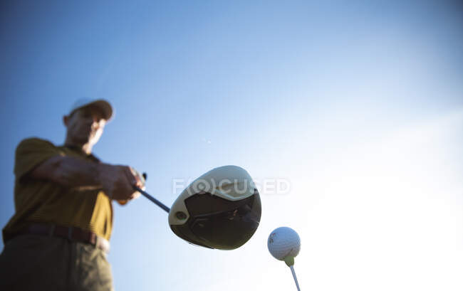 Vista frontale a basso angolo di un uomo caucasico in un campo da golf in una giornata di sole con cielo blu, che si prepara a colpire una palla — Foto stock
