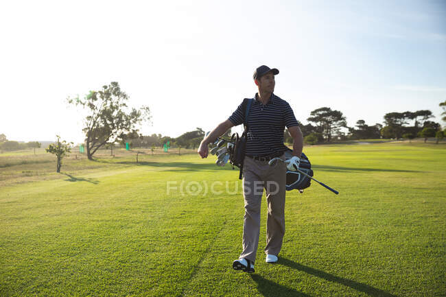 Вид спереди на кавказца на поле для гольфа в солнечный день с голубым небом, гуляющего и несущего сумку для гольфа — стоковое фото