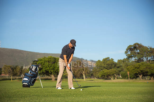 Vista frontale di un uomo caucasico in un campo da golf in una giornata di sole con cielo blu, che si prepara a colpire una palla — Foto stock