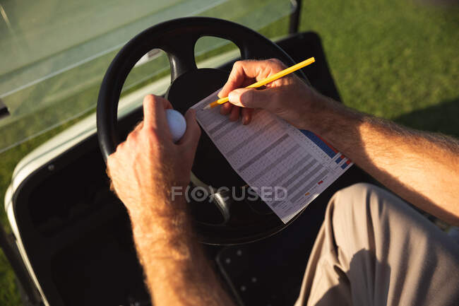 Крупним планом чоловік на полі для гольфу в сонячний день, пишучи рахунок на партитурі, сидячи в кошику для гольфу — стокове фото