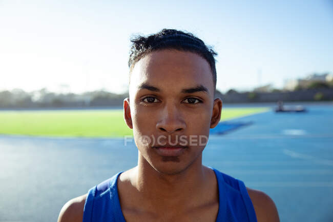 Portrait of a confident mixed race male athlete swearing a blue vest practicing at a sports stadium, looking straight to camera — Stock Photo