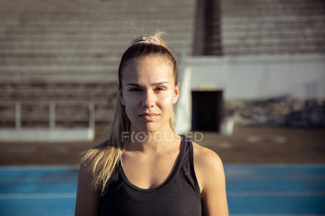 Retrato de uma atleta caucasiana confiante vestindo um colete preto praticando em um estádio de esportes, olhando para câmera e sorrindo — Fotografia de Stock