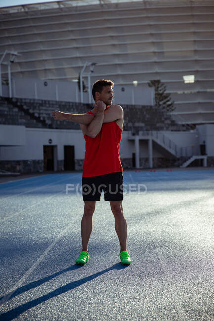 Вид спереди кавказского спортсмена, практикующего на спортивном стадионе, растянувшегося на беговой дорожке. — стоковое фото