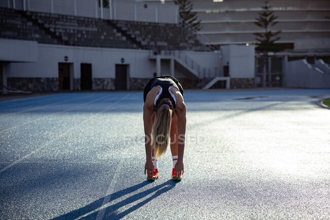 Передній погляд на кавказьку спортсменку, яка тренується на спортивному стадіоні, розтягується, згинається і торкається пальців ніг.. — стокове фото