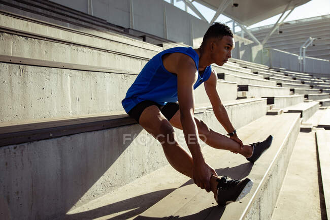 Вид збоку змішаної гонки спортсмен, який практикує на спортивному стадіоні, тягнеться на підставку, досягаючи щиколоток — стокове фото