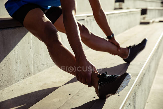 Side view low section of male athlete practicing at a sports stadium, sitting in the stands and stretching — Stock Photo