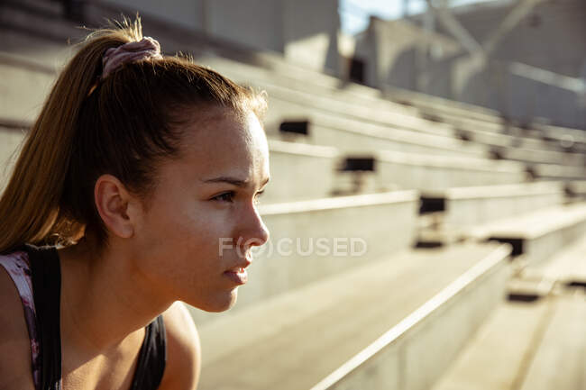 Vista lateral de cerca de una atleta caucásica practicando en un estadio deportivo, centrándose antes de una carrera. - foto de stock