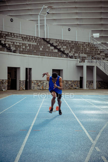 Vista frontal de un atleta masculino de raza mixta practicando en un estadio deportivo, corriendo hacia la cámara. - foto de stock