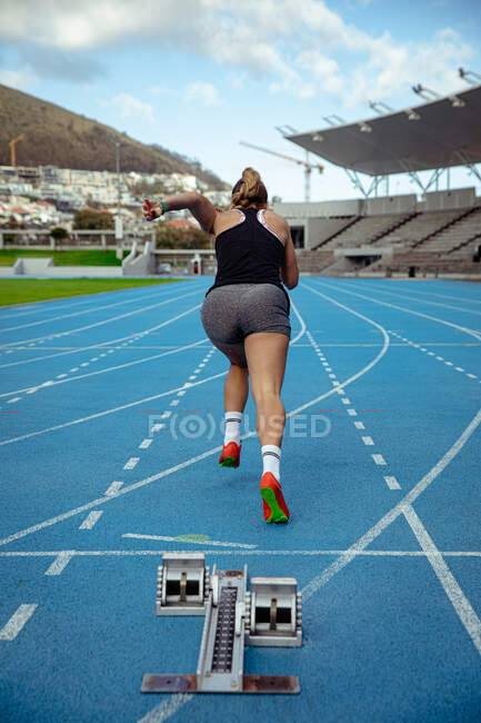 Передній вид кавказької спортсменки - спортсменки, яка тренується на спортивному стадіоні і біжить по біговій доріжці.. — стокове фото