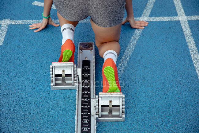 High angle close up of female athlete practicing at a sports stadium, in position on starting blocks, preparing to sprint — Stock Photo