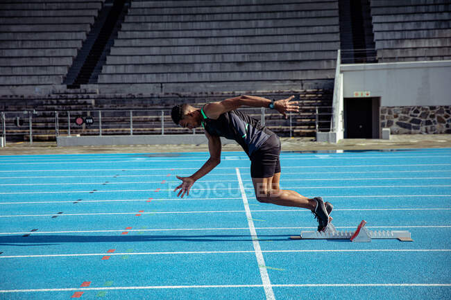 Side view of a mixed race male athlete practicing at a sports stadium, sprinting off the starting blocks at the beginning of a race — Stock Photo