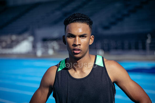 Portrait of a confident mixed race male athlete wearing a black vest practicing at a sports stadium, looking straight to camera — Stock Photo