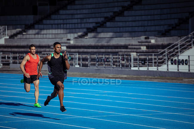 Side view of a Caucasian and a mixed race male athletes practicing at a sports stadium, racing each other on running track — Stock Photo