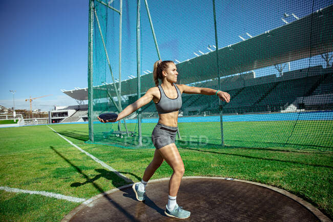 Vista laterale di un'atleta caucasica che pratica in uno stadio sportivo, preparandosi a lanciare un disco. — Foto stock