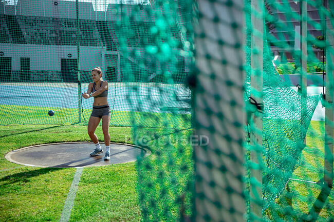 Vista lateral distante de uma mulher atleta caucasiana praticando em um estádio de esportes, preparando-se para jogar um martelo, foco seletivo — Fotografia de Stock