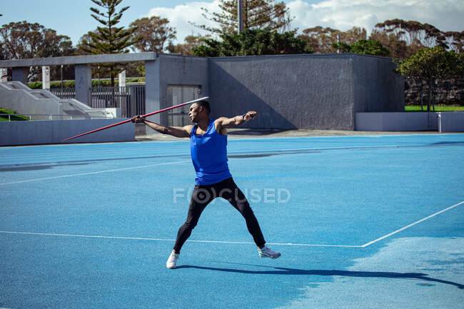 Vista lateral de um atleta mestiço praticando em um estádio de esportes, preparando-se para lançar um dardo. — Fotografia de Stock