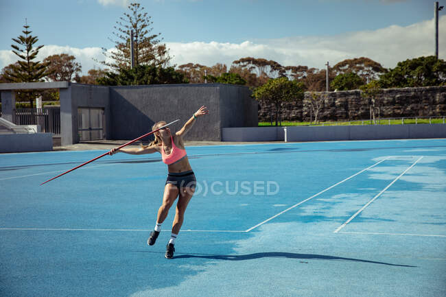 Vista lateral de una atleta caucásica practicando en un estadio deportivo, lanzando una jabalina. - foto de stock