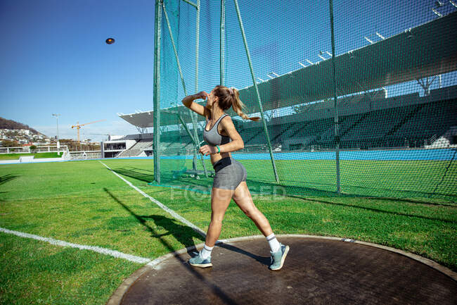 Vista lateral de una atleta caucásica practicando en un estadio deportivo, lanzando un disco. - foto de stock
