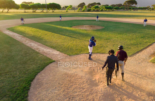 Беспилотный снимок бейсбольной команды, играющей в бейсбол на бейсбольном поле в солнечный день, виден из-за ловца — стоковое фото