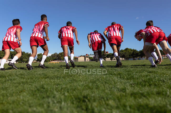 Низький кут огляду підліткової багатоетнічної чоловічої команди регбістів, які носять командну смугу, бігають разом у ігровому полі . — стокове фото