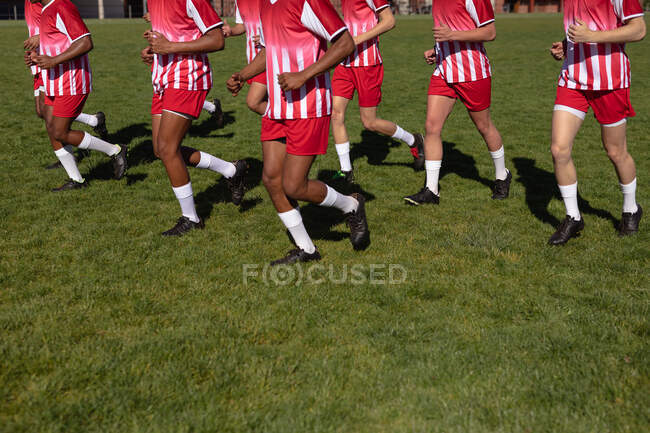 Vista laterale bassa sezione della squadra maschile di giocatori di rugby che indossano la loro striscia di squadra, correndo insieme sul campo di gioco. — Foto stock