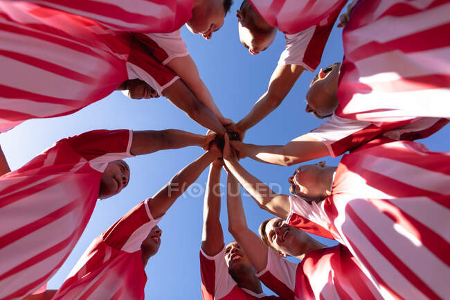 Low angle view of a teenage multi-ethnic male team of rugby players wearing their team strip, stacking hands and smiling. — Stock Photo