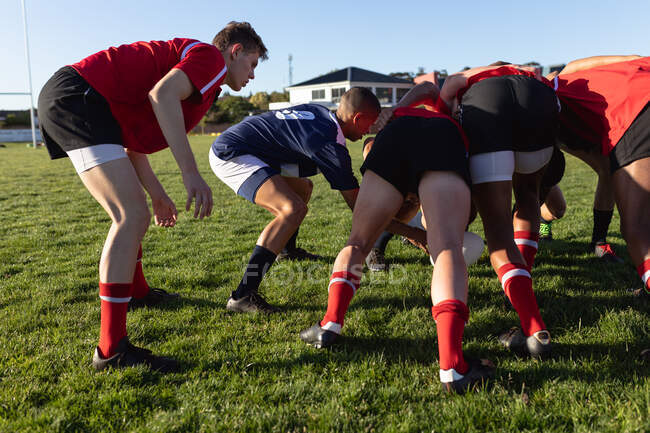 Rückansicht von zwei multiethnischen Männerteams mit Rugby-Spielern, die ihre Mannschaftsstreifen tragen, in einem Gedränge auf einem Spielfeld während eines Rugbyspiels darauf warten, dass der Ball verteilt wird — Stockfoto