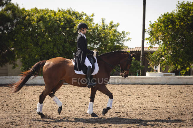 Vista lateral de um cavaleiro de curativo feminino caucasiano inteligentemente vestido montando um cavalo castanho durante o show de curativo em um dia ensolarado . — Fotografia de Stock