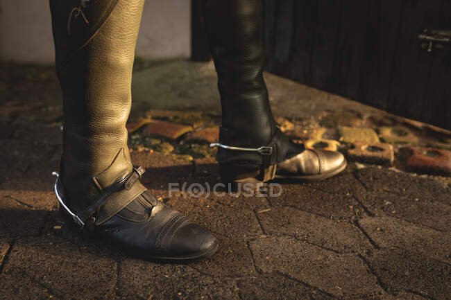 Visão lateral seção baixa de um homem inteligentemente vestido usando botas de equitação e esporas, em pé por um estábulo de equitação em um dia ensolarado. — Fotografia de Stock