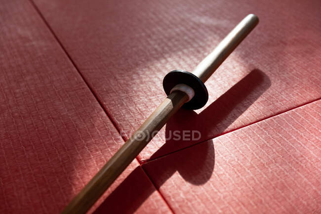 High angle close up view of a wooden judo jo stick lying on red gym mats in sports hall during judo training. — Stock Photo