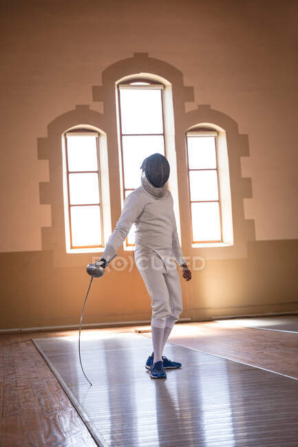 African American sportsman wearing protective fencing outfit during a fencing training session, preparing for a duel, holding an epee. Fencers training at a gym. — Stock Photo