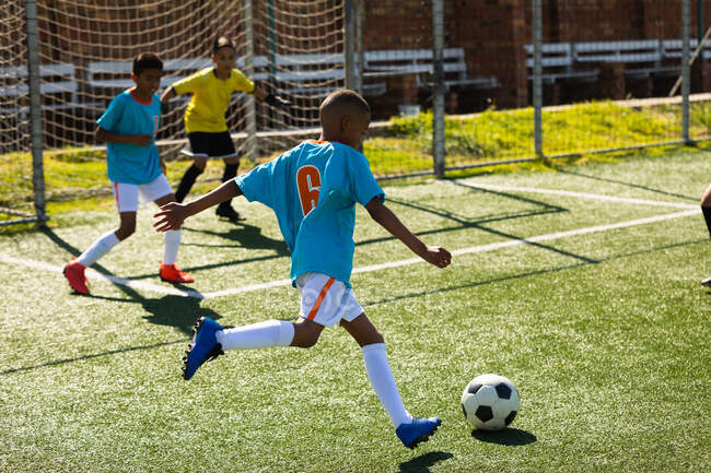 Side view of two multi-ethnic teams of boy of soccer wearing their team strips, in action during a soccer match on a playing field, on mixed race boy about to take a shot at goal — Stock Photo