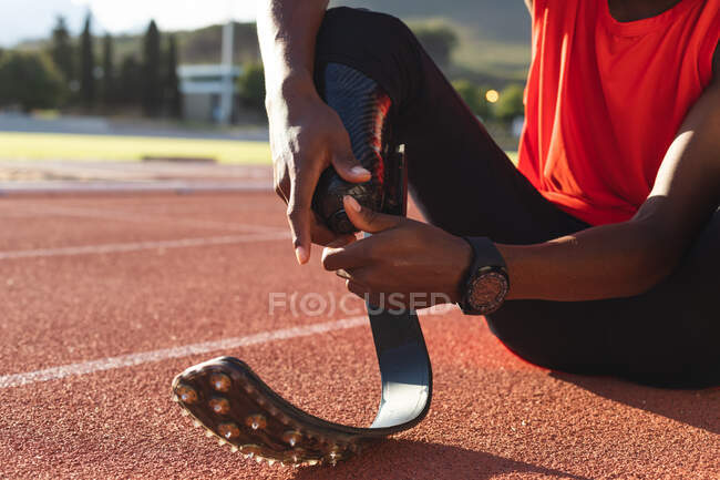 Mid section of fit, disabled male athlete at an outdoor sports stadium, sitting on race track adjusting running blades. Disability sport training. — Stock Photo