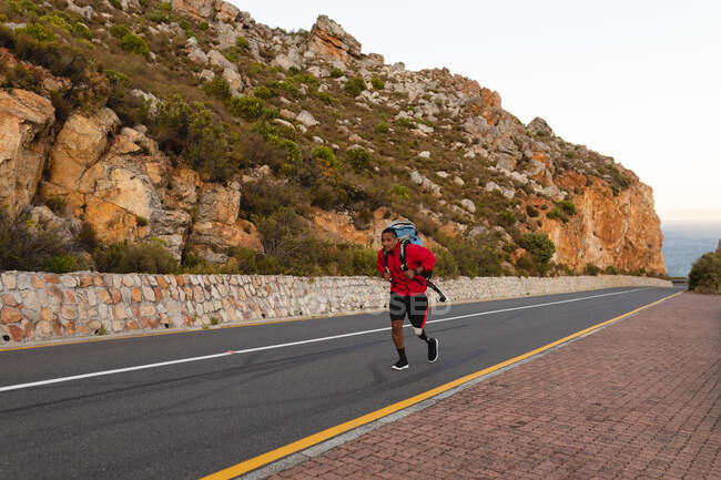 Athlète masculin en forme, handicapé, de race mixte avec une jambe prothétique, profitant de son temps sur un voyage à la montagne, randonnée, marche sur la route par la mer. Mode de vie actif avec handicap. — Photo de stock