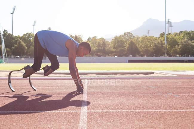 Fit, mixed race disabled male athlete at an outdoor sports stadium, starting a race on race track wearing running blades. Disability athletics sport training. — Stock Photo