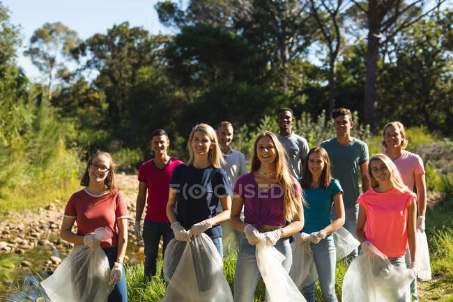 Retrato de un grupo multiétnico de voluntarios de conservación limpiando el río en el campo, sonriendo a la cámara sosteniendo sacos de basura. Ecología y responsabilidad social en el medio rural. - foto de stock