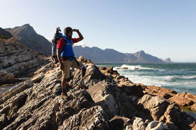 A fit, disabled mixed race male athlete with prosthetic leg, enjoying his time on a trip to the mountains, hiking, admiring the view of the sea. Active lifestyle with disability. — Stock Photo