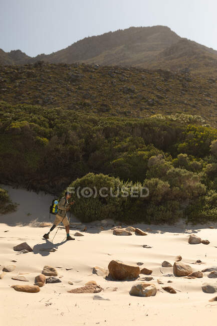 Um atleta masculino de raça mista, apto, com perna protética, aproveitando seu tempo em uma viagem para as montanhas, caminhando com paus, andando na praia à beira-mar. Estilo de vida ativo com deficiência. — Fotografia de Stock